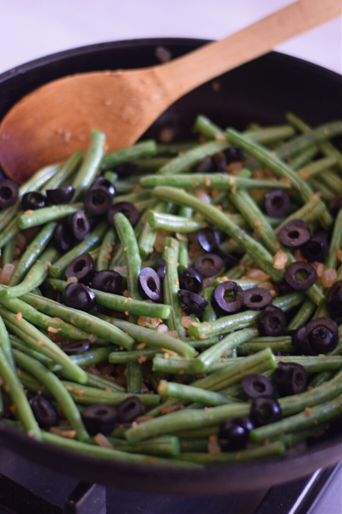 Green beans with black olives in a skillet.