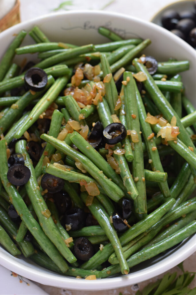 Sauteed green beans with black olives in a white bowl.