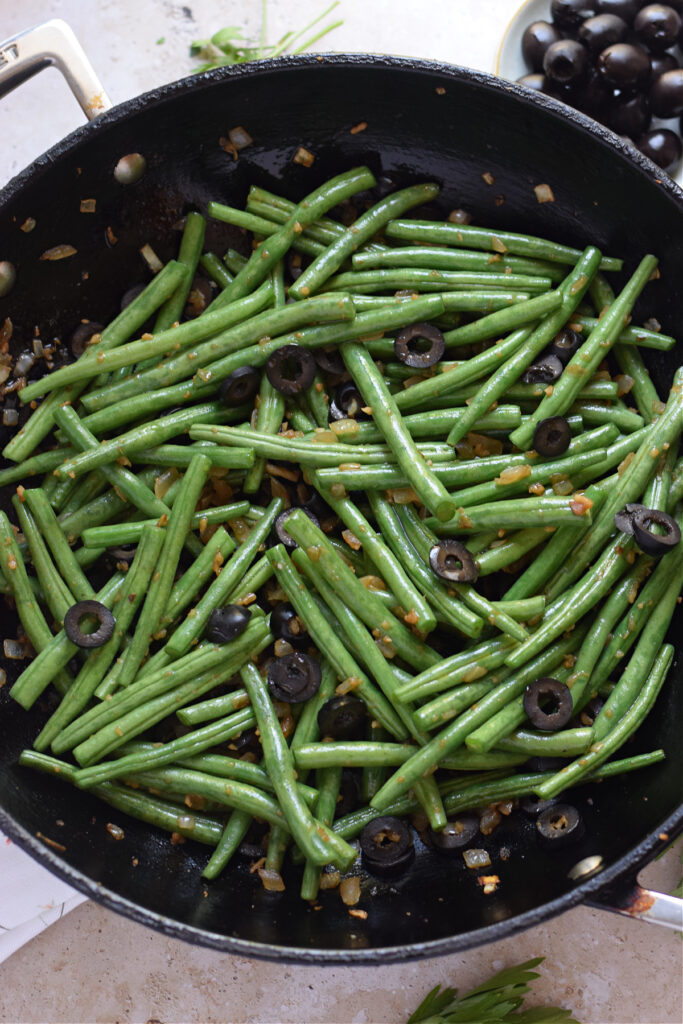 Green beans with black olives in a skillet.
