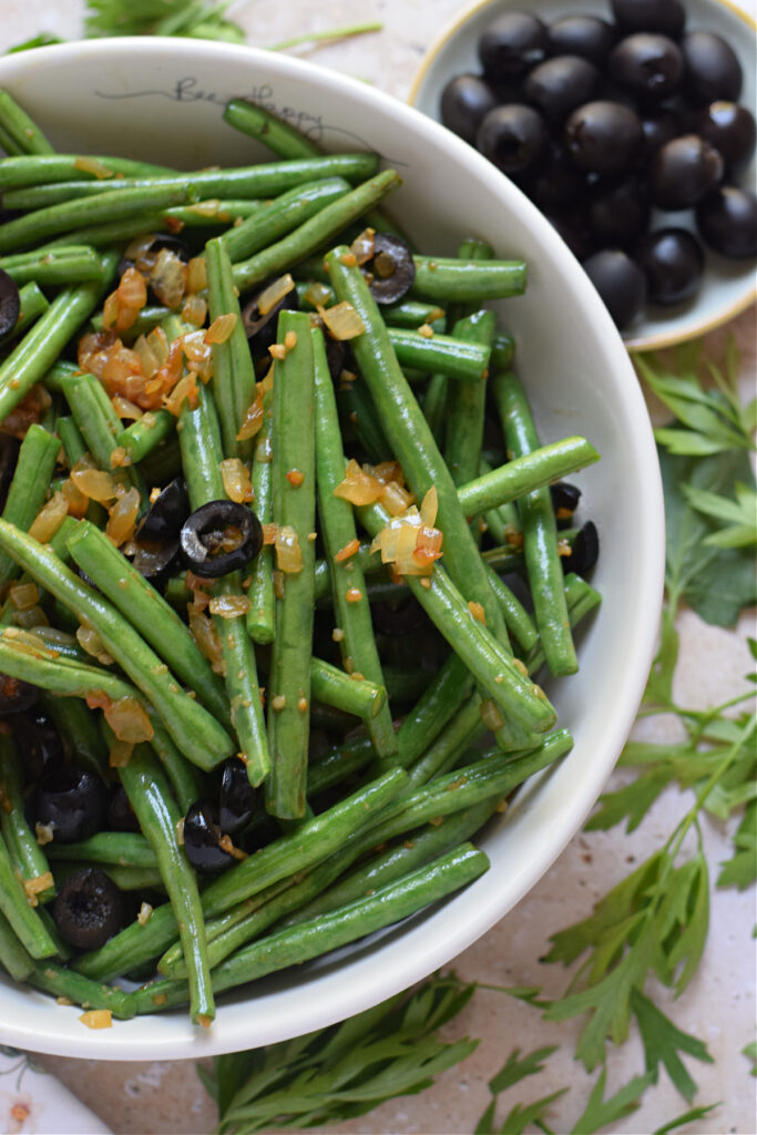 Close up of sauteed green beans with black olives.