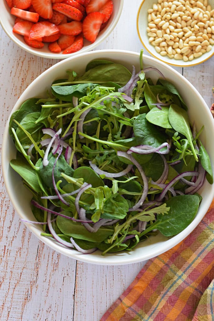 Making a green salad with red onions and spinach in a white bowl.
