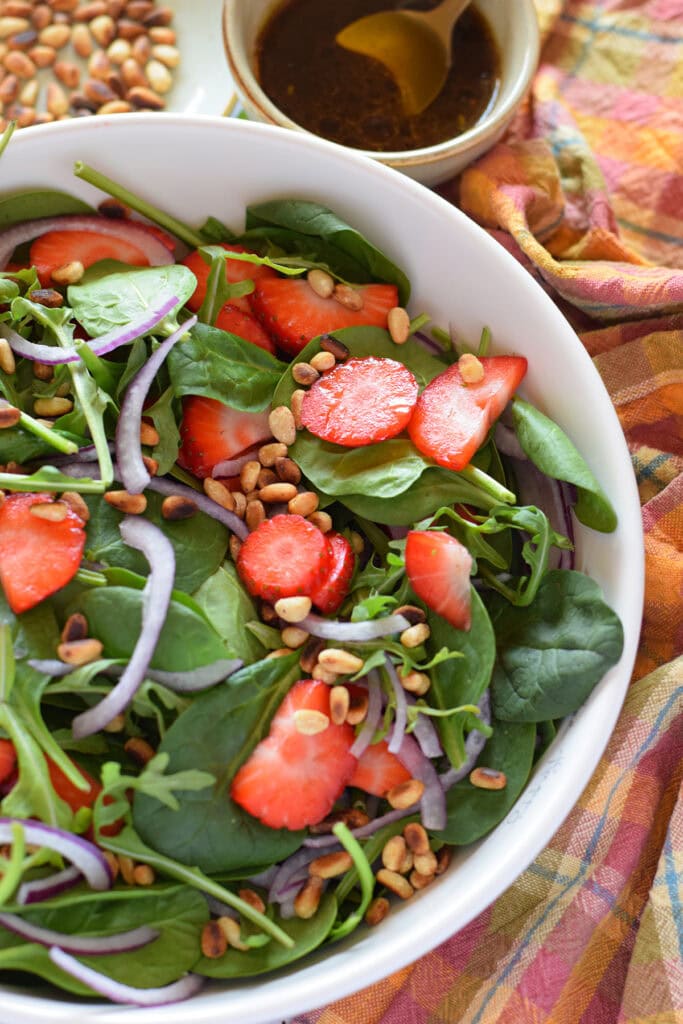 spinach and strawberry salad in a white bowl.