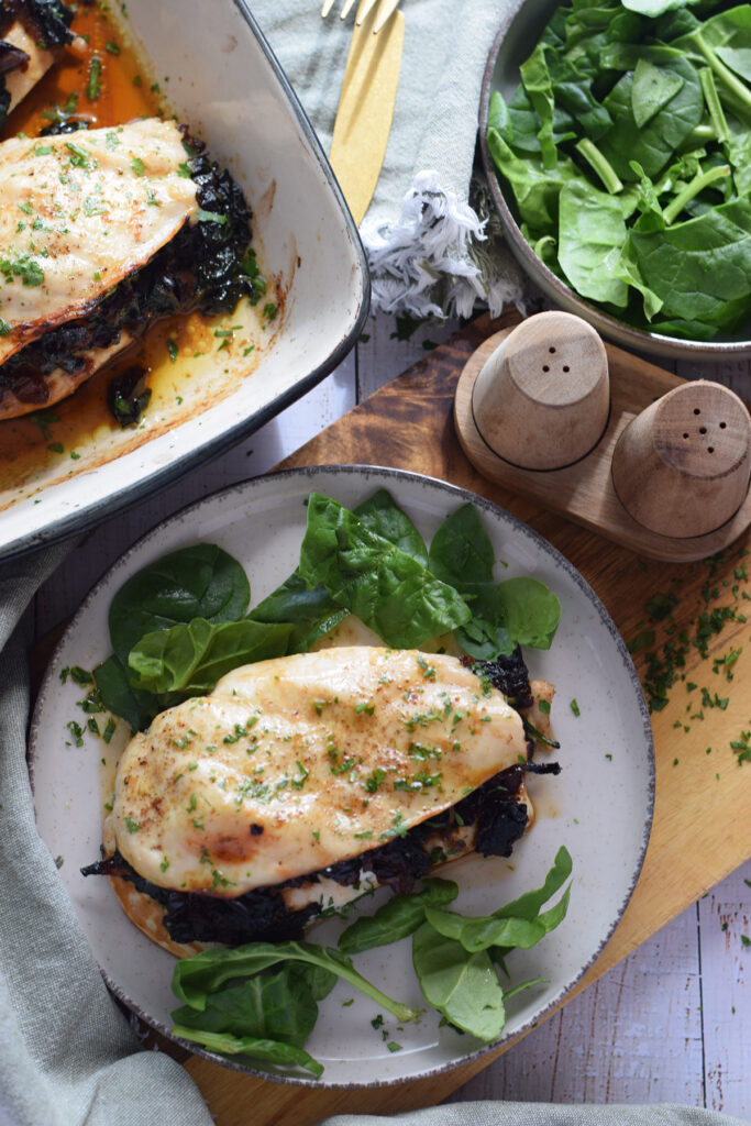 Stuffed chicken on a plate with spinach and caramelized onions.
