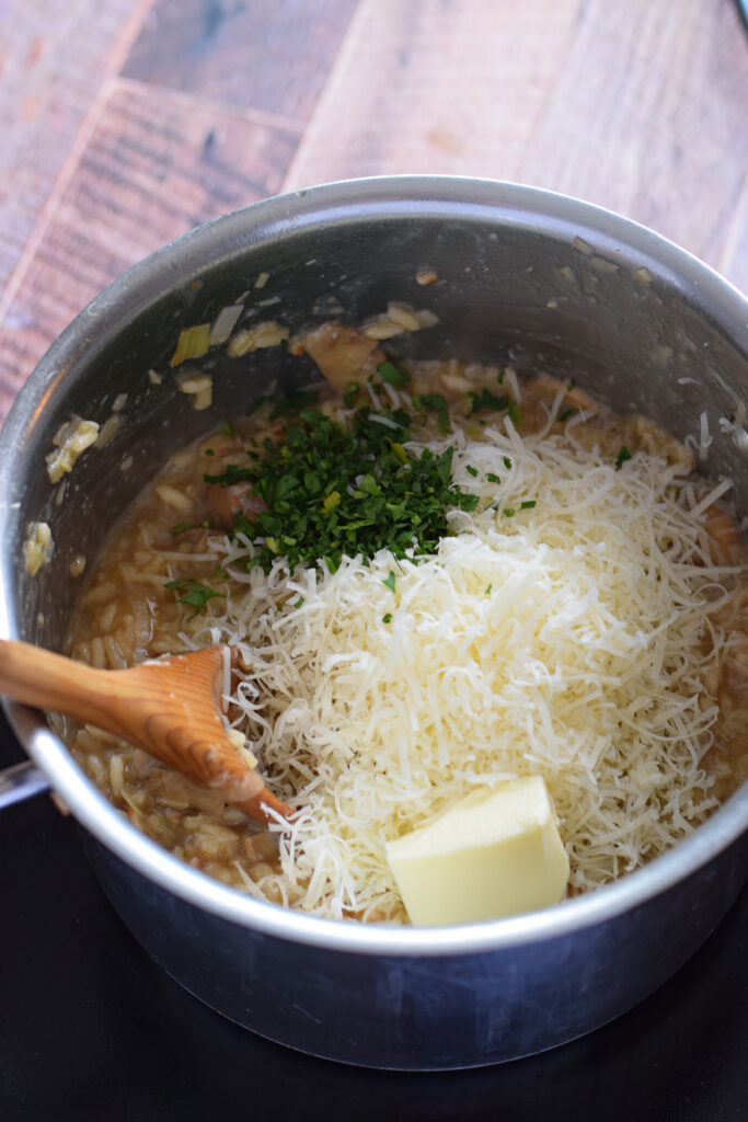 Adding cheese, parsley and butter to risotto in a saucepan.