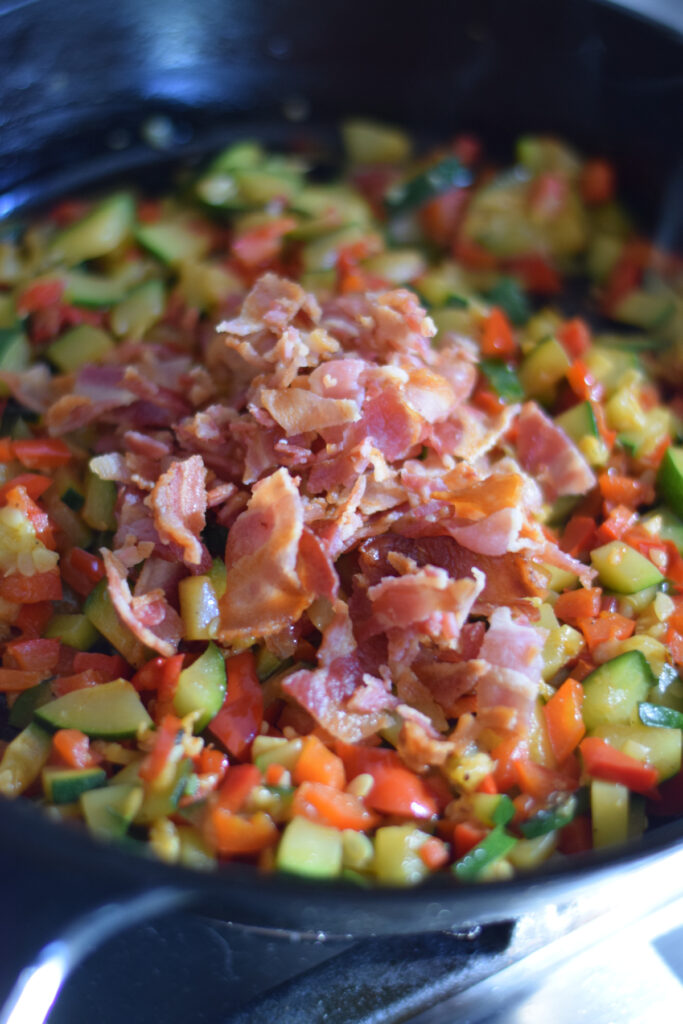 Adding bacon to vegetables in a skillet.