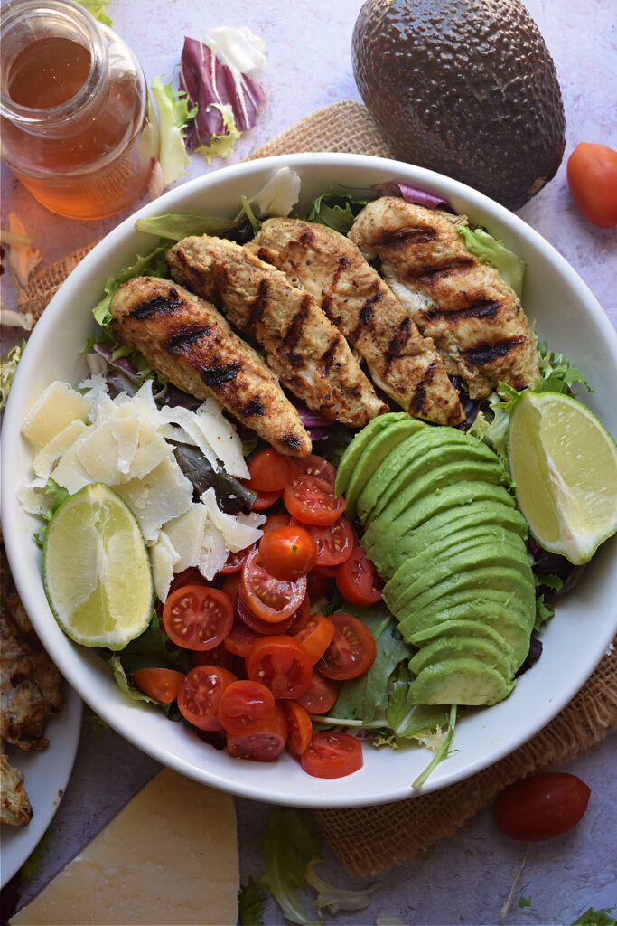 Chicken tenders in a bowl with avocado, tomatoes and lettuce.