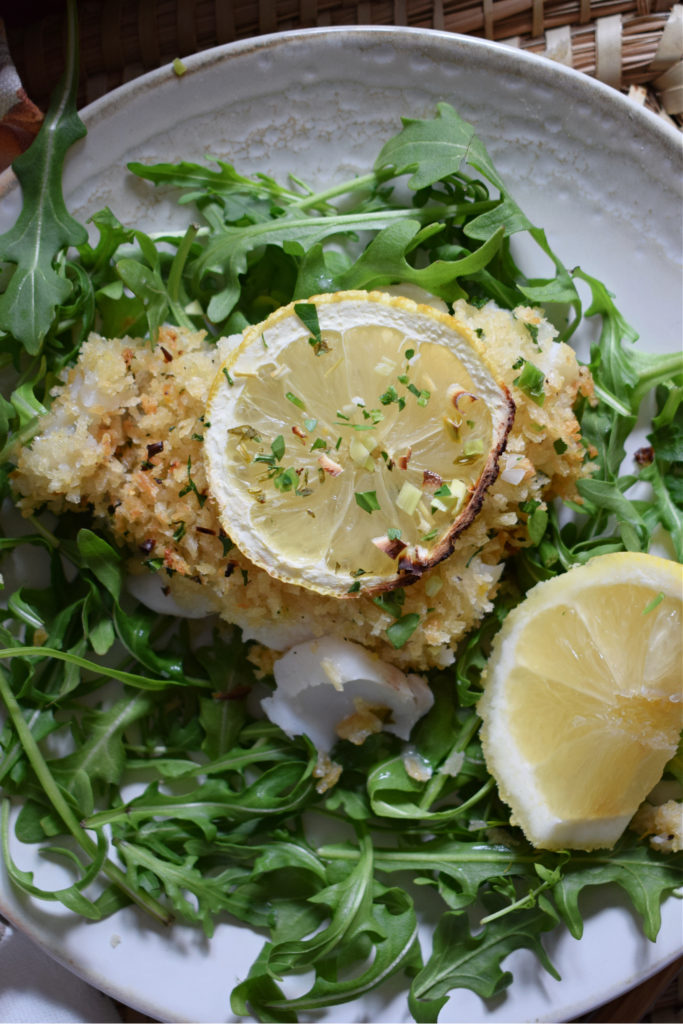 over head view of lemon crusted baked cod with arugula and lemon slices
