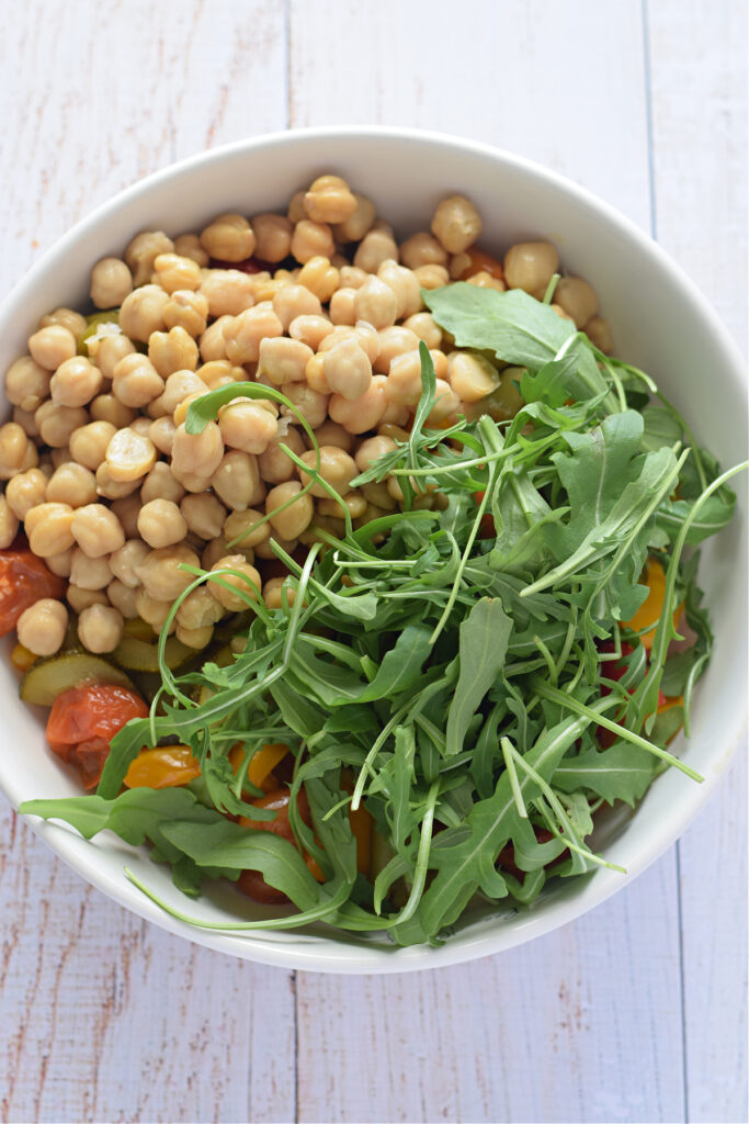 Adding chickpeas and arugula to a mediterranean salad.