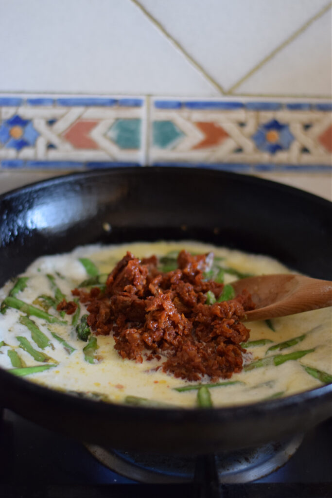 Adding sun dried tomatoes to a creamy pasta sauce.