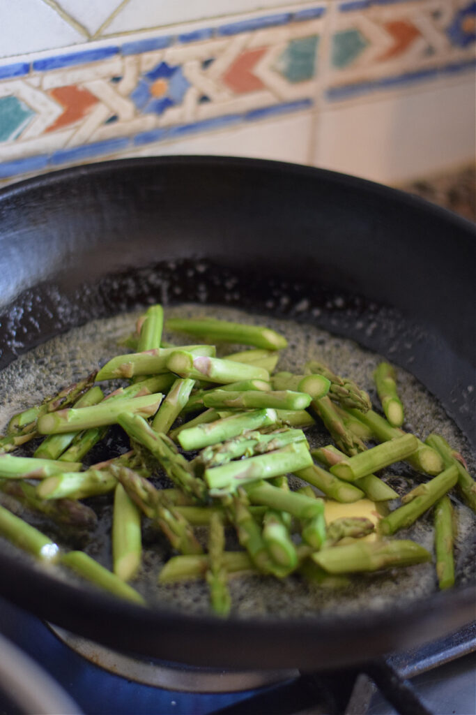Adding asparagus to a cast iron skillet.
