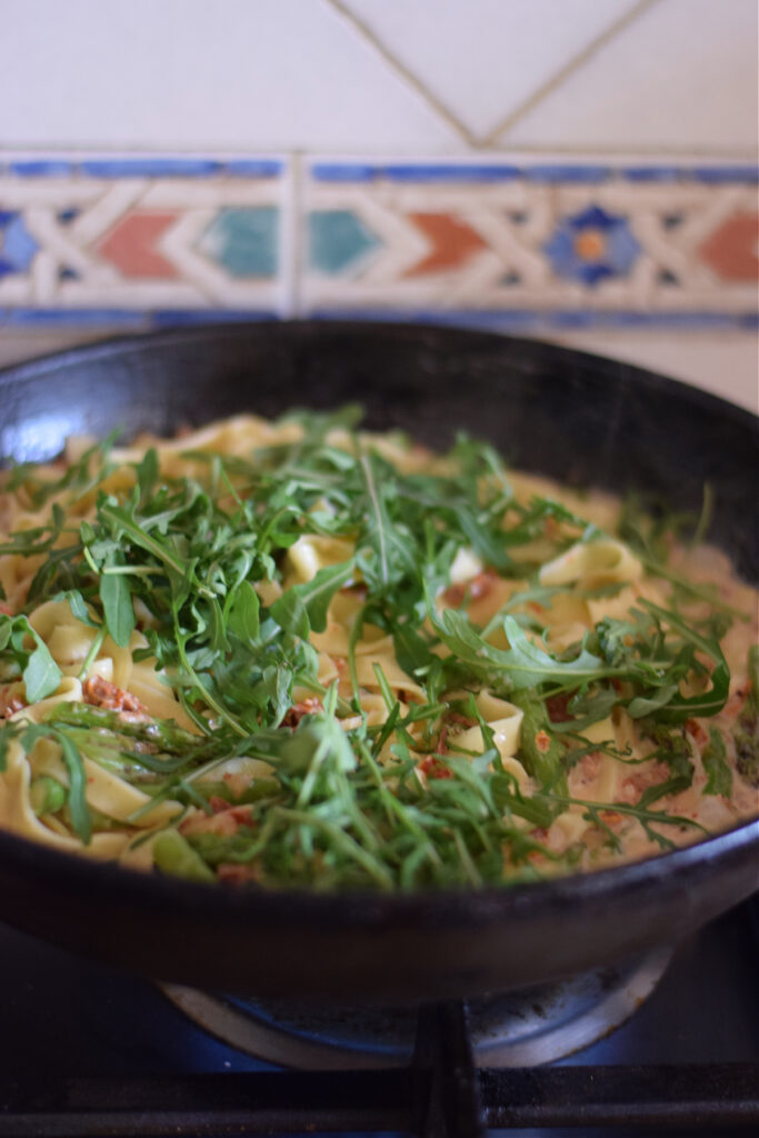 Adding arugula to a pasta dish.
