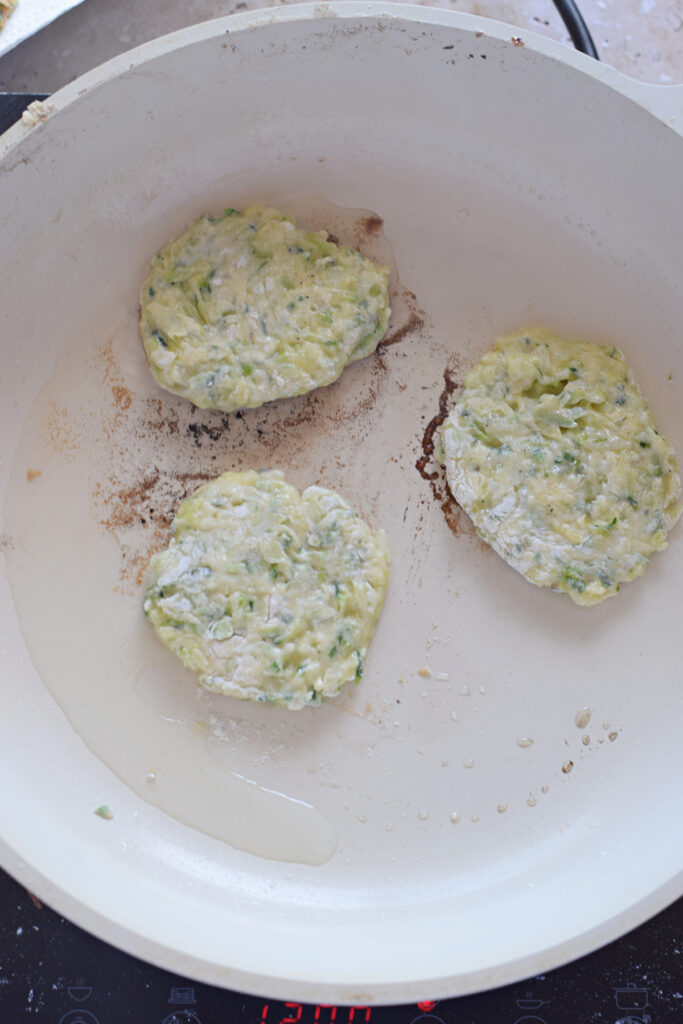 Cooking zucchini fritters in a white skillet.