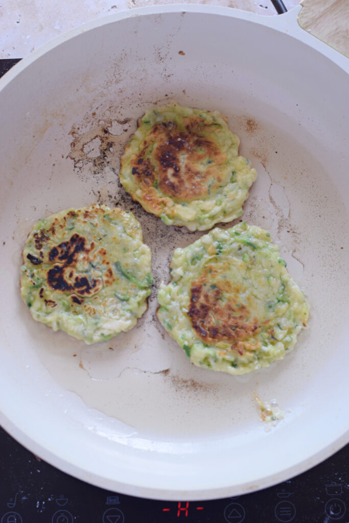 Cooking zucchini fritters in a skillet.