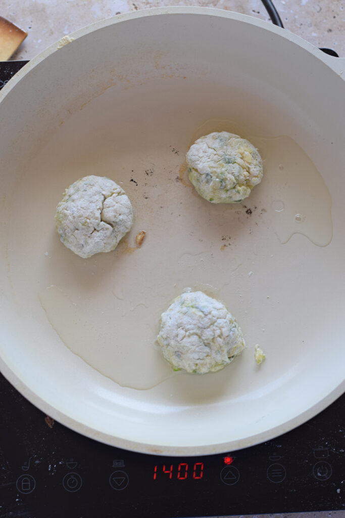Cooking zucchini fritters in a skillet.