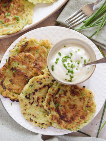 Zucchini fritters on a white plate with a serving sauce.
