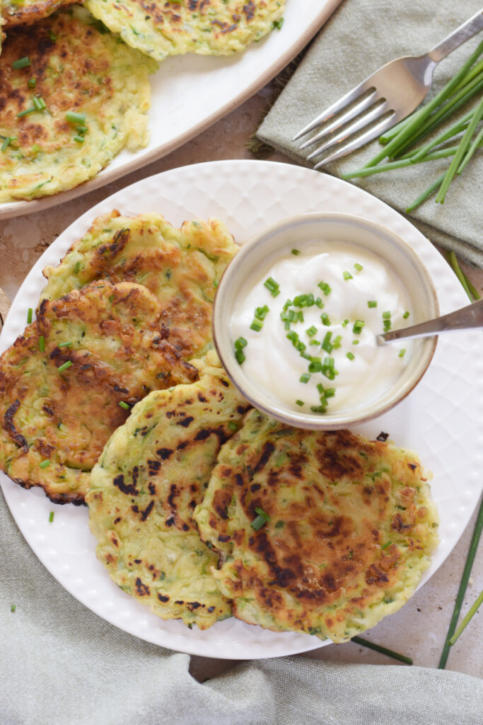 Zucchini fritters on a white plate with a serving sauce.