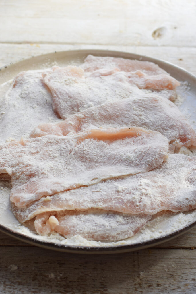 Chicken cutlets coated in flour on a plate.