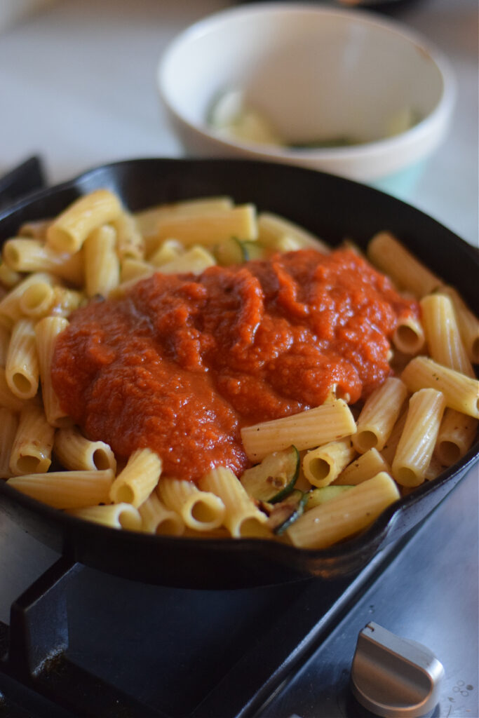 Adding pasta sauce to a skillet with pasta.