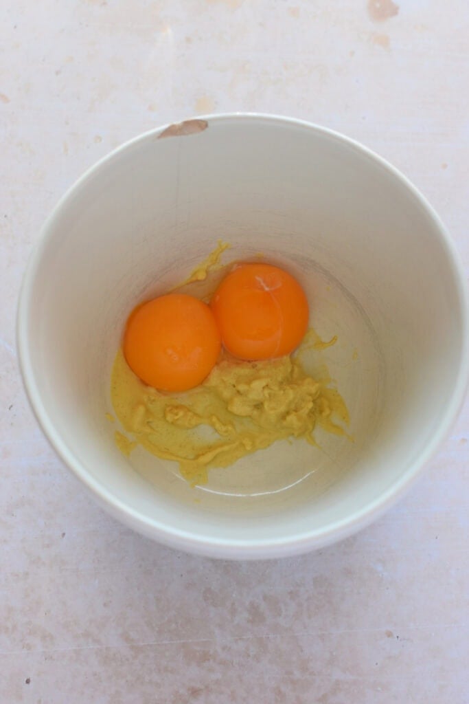 Adding egg yolks to garlic and mustard.