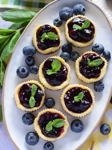 Mini blueberry cheesecakes on a white oval plate.