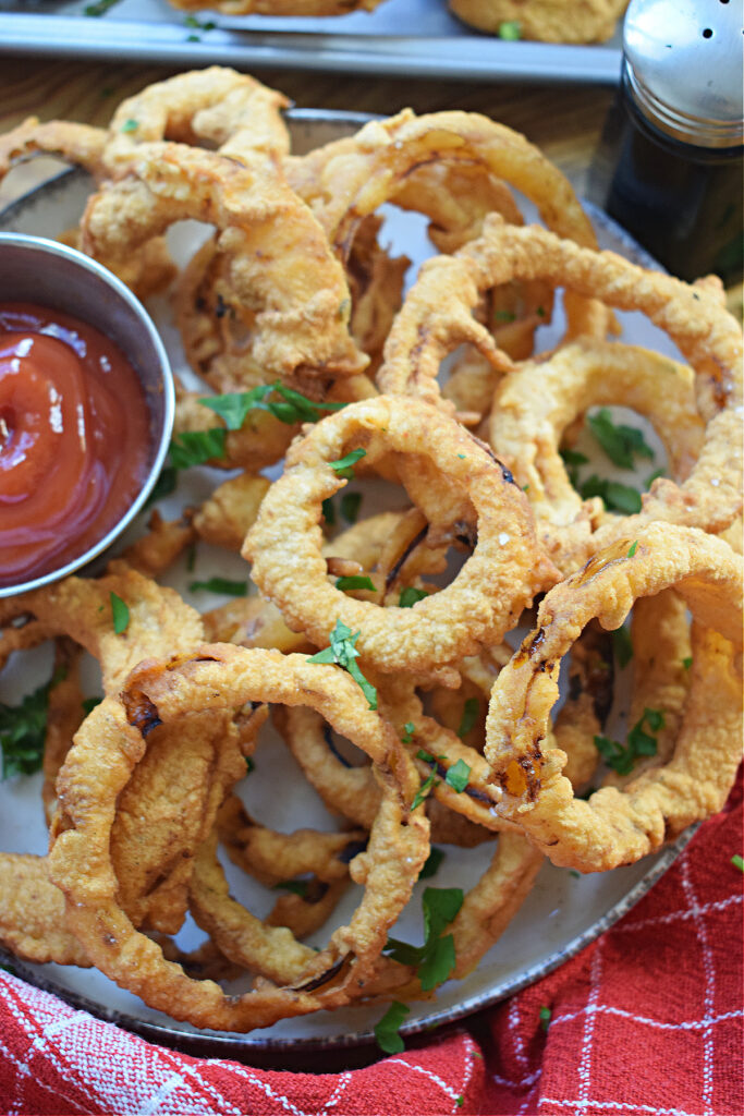 Beer battered onion rings on a plate with a sauce in a small dish.