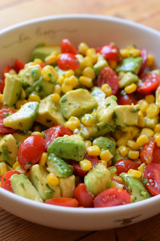 A tossed avocado corn and tomato salad in a bowl.