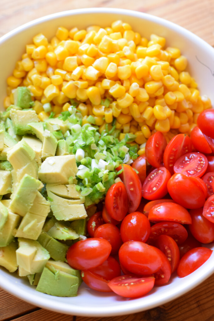 Ingredients in a bowl to make an avocado tomato and corn salad.