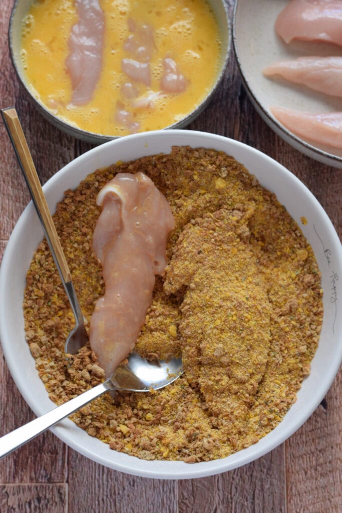 Dipping chicken tenders in bread crumbs.