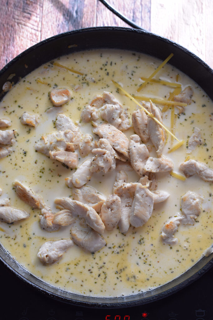 Adding chicken and pasta to a skillet.
