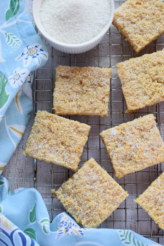 Coconut bars on a cooling rack with a blue tea towel.