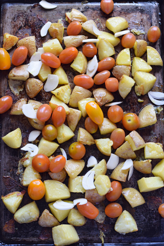 Adding cherry tomatoes and garlic to roasted potatoes.