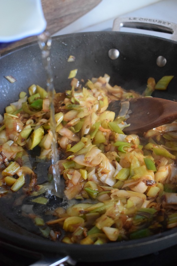 Adding wine to cooked leeks in a skillet.