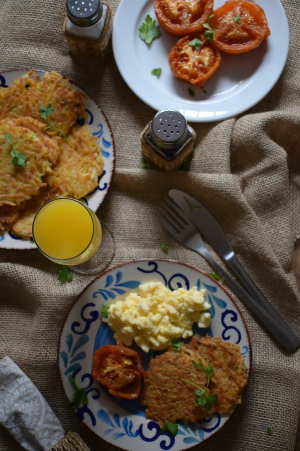 overhead table setting view of hash browns with juice, eggs and tomato