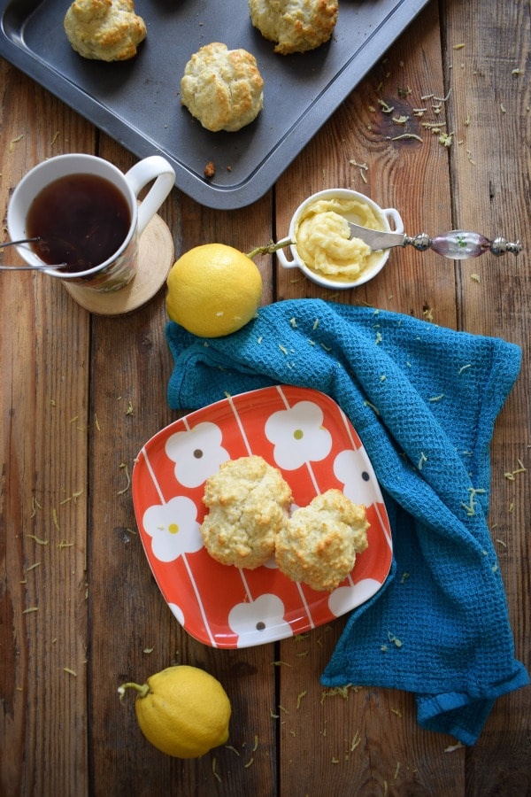 Table setting of Lemon scones with ab baking tray, cup of tea, lemons, butter and a tea towel