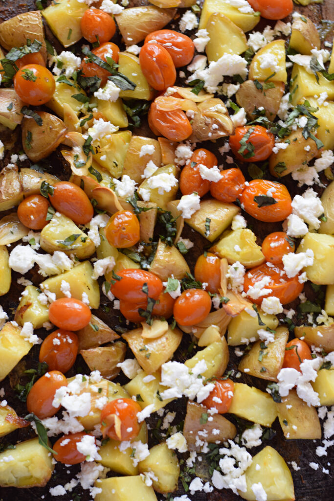 Roasted potatoes with tomatoes and feta on a baking tray.
