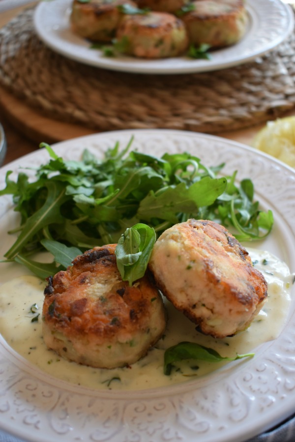 Close up of Salmon and Leek Cakes with sauce and salad leaves.