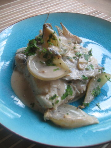 simmered hake & baby onions in a white wine sauce on a blue plate