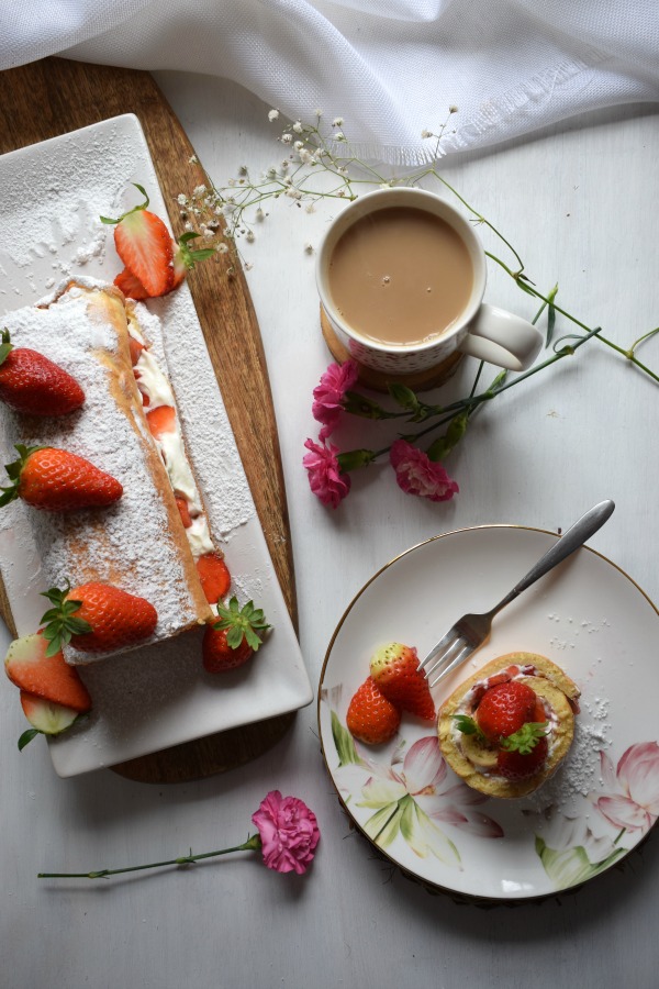 Table setting of the Strawberry & Cream Swiss Roll Cake with a cup of coffee and flowers image