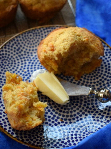 a buttery carrot muffin on a blue plate with butter