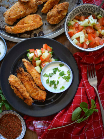 Cajun chicken tenders on a plate with a dip and a salad.