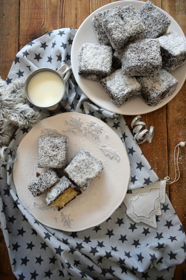 Lamingtons on a wooden table top with a cup of milk.