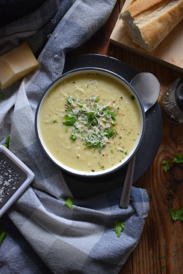 over head view of potato and leek soup with a tea towel, bread and a spoon