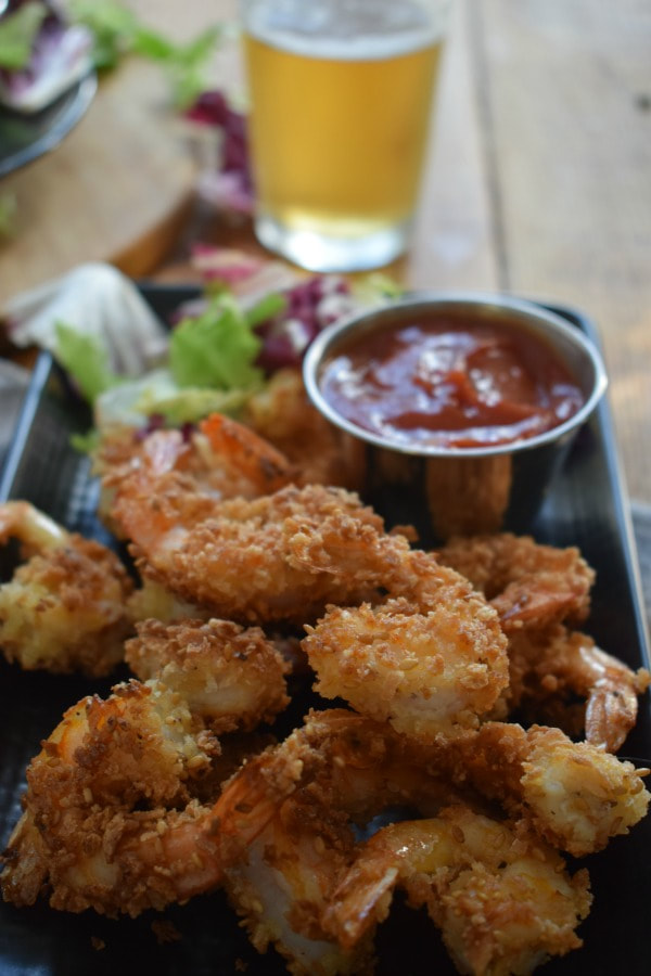 Sesame and Panko Crusted Fried Shrimp on a plate with a dipping sauce and a drink in the background