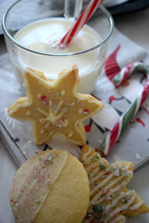 butter cream topped sugar cookies with a glass of milk and a candy cane