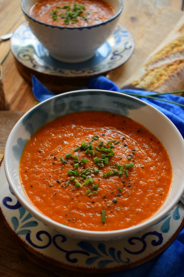 Roasted tomato soup topped with chives in a white and blue bowl