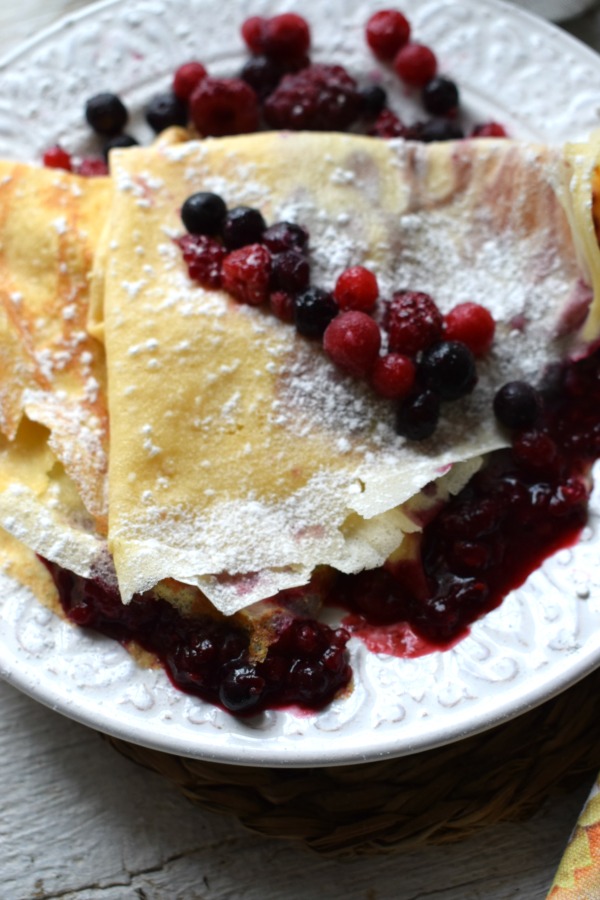 Wild berry compote crepes on a white plate.