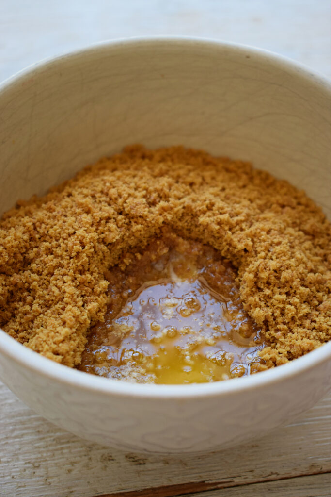 Making a cheesecake base of cookie crumbs and melted butter in a bowl.