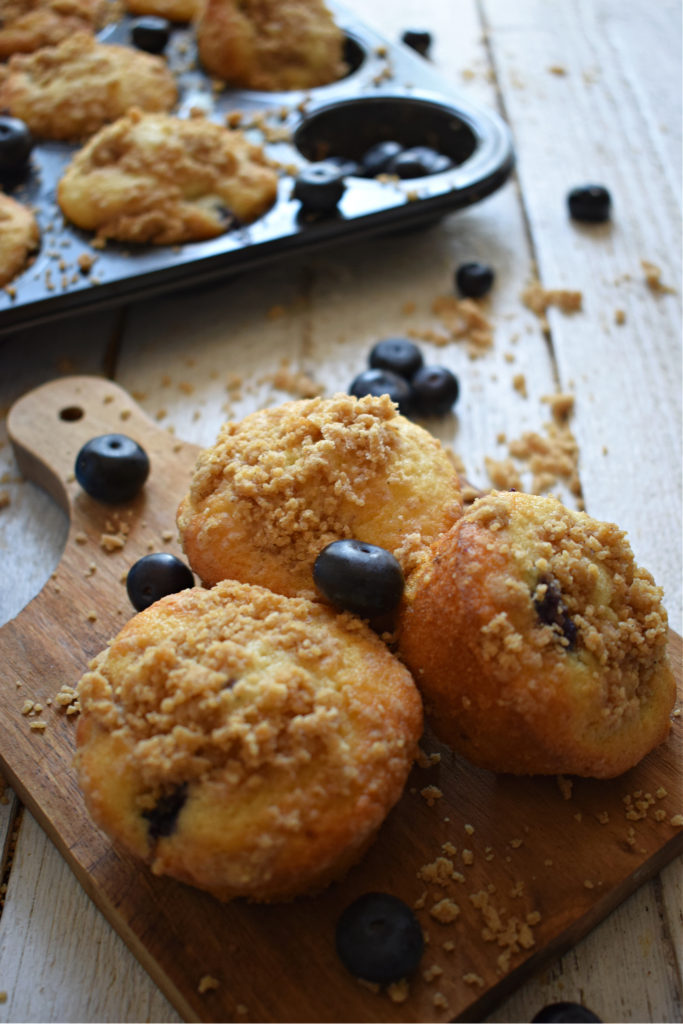 Blueberry strudel muffins on a wooden board with muffins in the background and extra blueberries