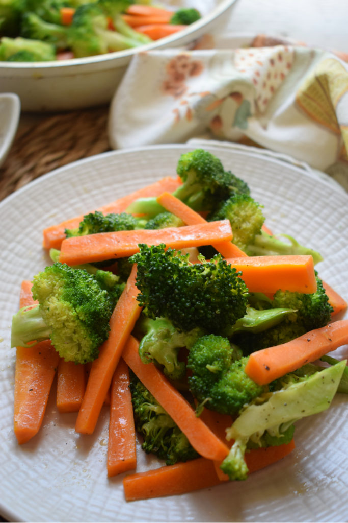 Broccoli & Carrots on a plate with a serving dish and napkin in the background