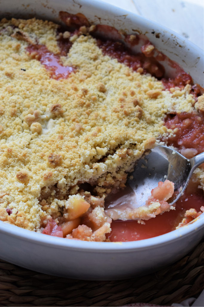 Apple and strawberry crumble in a baking dish with a large spoon